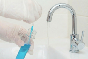 A gloved scientist tests tap water quality by taking a sample with a pipette from a test tube.